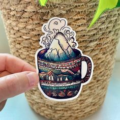 a hand holding a sticker with a mountain in a cup