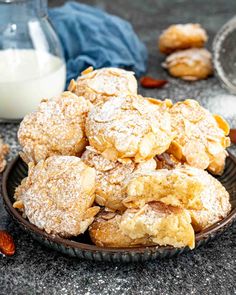 powdered sugar cookies piled on top of each other in a bowl next to a glass of milk