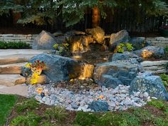 a garden with rocks, water and plants in the center is lit up by lights