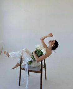 a woman sitting on a chair with flowers in her lap and arms stretched out to the side