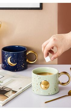 a person is holding a white paper in front of a coffee cup with gold handles