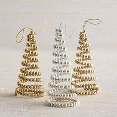 three christmas trees made out of beads on a white tablecloth with gold and silver ornaments