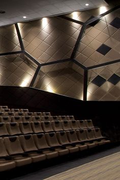 an empty auditorium with rows of seats and lights on the ceiling, in front of a tiled wall