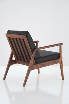 a wooden chair with black cushion on it's back and arm rests against a white wall