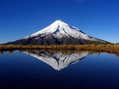 a snow covered mountain is reflected in the still water on a clear, sunny day