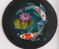 a painting of two koi fish and a pink flower on a black circular plate