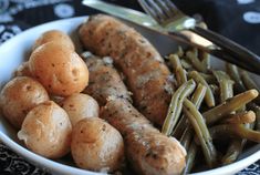 a white bowl filled with potatoes and green beans next to a fork on top of a table