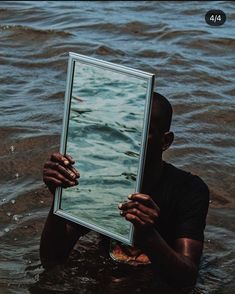 a man holding up a mirror in the water