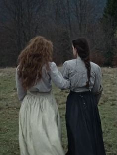 two women in long dresses walking through a field