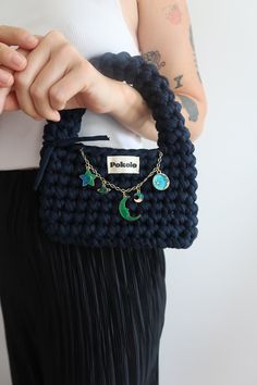 a woman holding a crocheted purse with charms on it's handles and chain