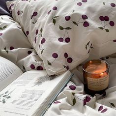 an open book sitting on top of a bed next to a candle