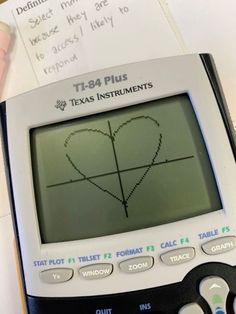 a calculator with a heart drawn on the screen next to some writing paper