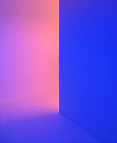 an empty room with blue and pink lighting on the walls, in front of a white wall