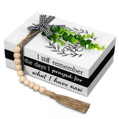 a white box with a tassel and some green leaves on it next to a wooden beaded necklace