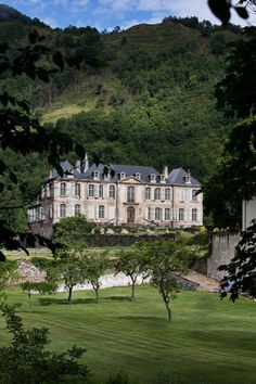 an old mansion in the middle of a lush green field with trees and mountains behind it