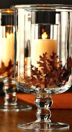 candles are lit in clear glass vases with leaves on the rim and inside them