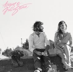 a man and woman sitting next to each other on top of a brick wall together