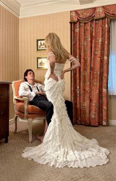 a woman in a white wedding dress standing next to a man sitting on a chair