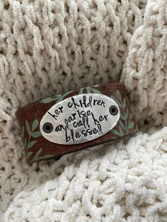 a brown and white bracelet with writing on it sitting on top of a knitted blanket