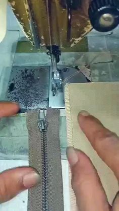 two hands are working on a piece of fabric with a sewing machine in the background