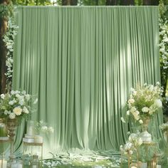 an outdoor wedding setup with green drapes and white flowers on the side, surrounded by gold vases