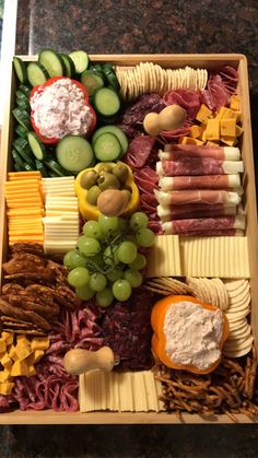 an assortment of cheeses, meats and vegetables arranged in a wooden platter