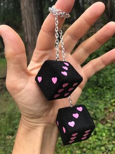 a hand holding two black dices with pink hearts hanging from it's sides