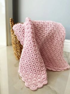 a pink crocheted blanket sitting on top of a table next to a basket