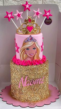 a pink and gold birthday cake with barbie on it's top, surrounded by stars