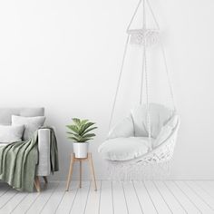 a white room with a hanging chair, potted plant and blanket on the floor