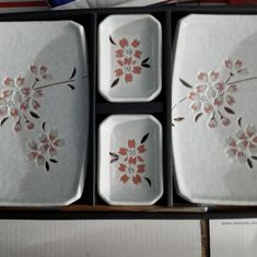 four white dishes with pink flowers on them in a black box next to an american flag