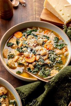 two bowls of vegetable soup on a wooden table next to bread and green mitts