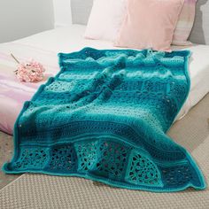 a crocheted blanket sitting on top of a bed next to pillows and flowers