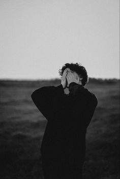 black and white photograph of a person covering their face with his hands while standing in an open field