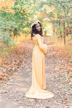 a pregnant woman in a yellow dress standing on a path with leaves all around her