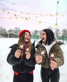 two girls holding sparklers in their hands and smiling at each other while standing in the snow