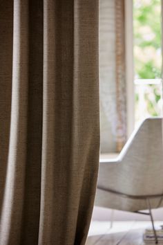 a chair sitting in front of a window with curtains on the outside and an open window behind it