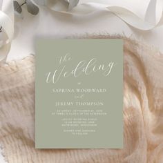 a wedding card on top of a blanket next to some white flowers and greenery