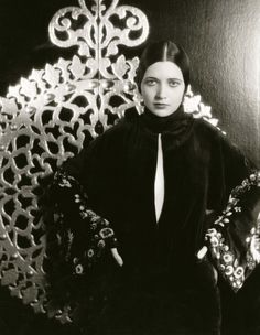 an old black and white photo of a woman in front of a wall with intricate designs