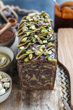 a loaf of chocolate cake sitting on top of a wooden table next to bowls and spoons