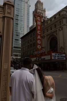 a man and woman standing next to each other in front of the chicago theater sign