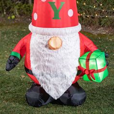 an inflatable santa clause sitting on the grass with a green present under his leg