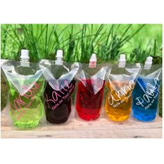 six different colored water bottles sitting on top of a wooden table next to green grass