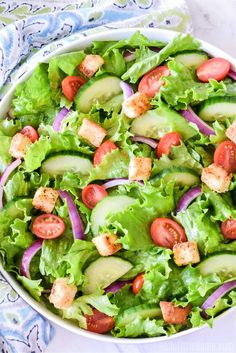 a salad with cucumbers, tomatoes and croutons in a white bowl