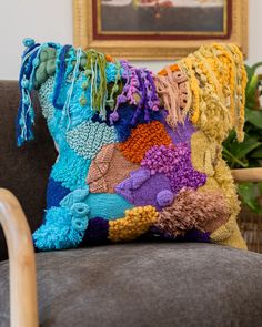 a multicolored crocheted pillow sitting on top of a gray couch next to a painting