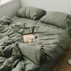 an unmade bed with green sheets, pillows and a book on the floor next to it