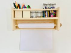 a roll of paper is hanging on the wall next to a shelf with pens, pencils and markers