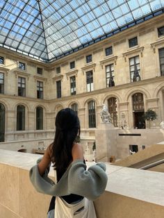 a woman standing in front of a building looking up at the sky with a glass roof