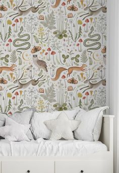 a white bed sitting under a wallpaper covered in animals and plants on top of it