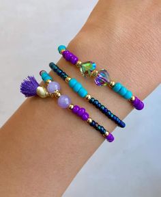 three different bracelets with beads and tassels on the wrist, one is purple